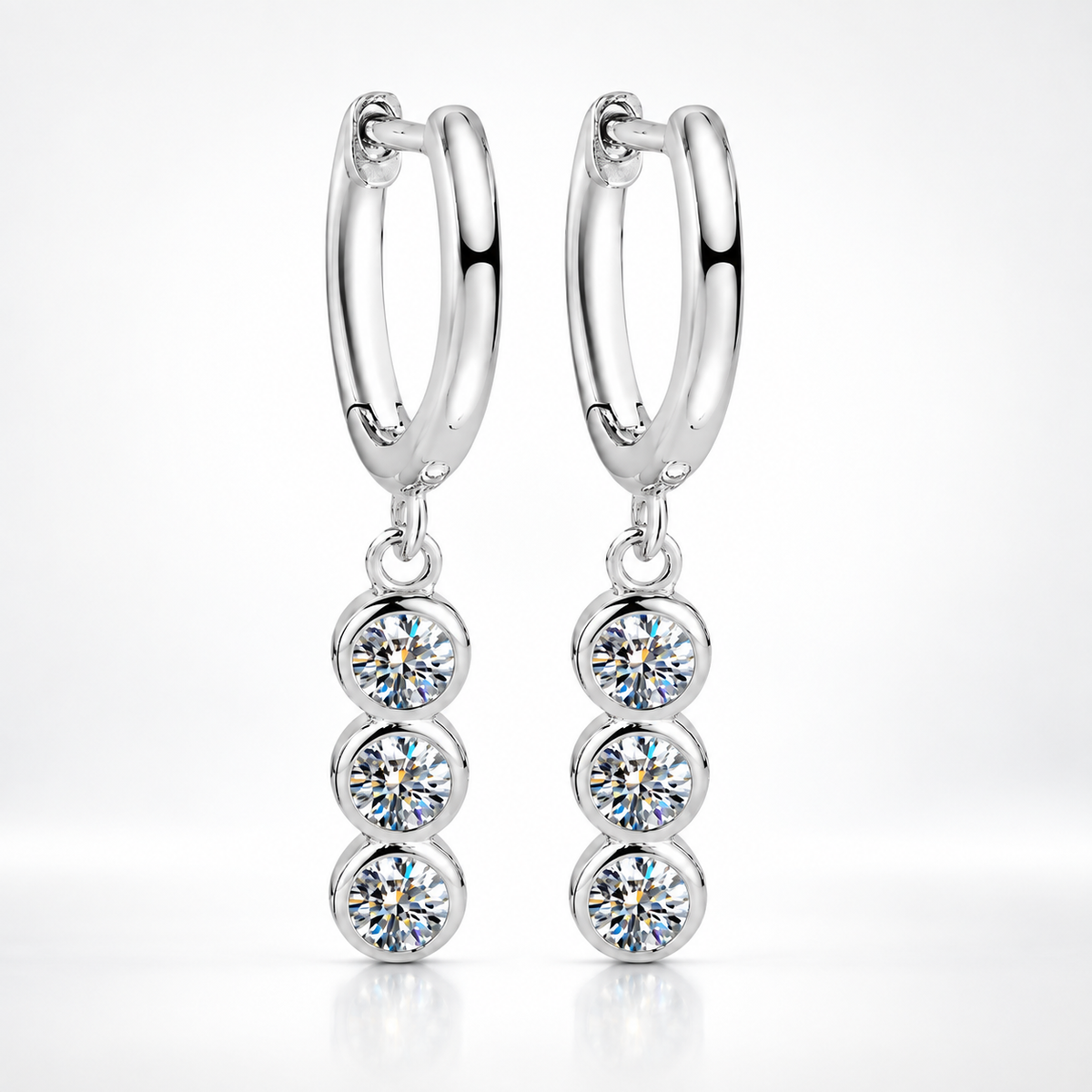 Silver huggie hoop earrings with three bezel-set round moissanite drops on a white background