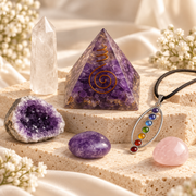 Holistic crystal wellness collection featuring an amethyst pyramid, quartz point, amethyst geode, chakra pendant, rose quartz and polished amethyst on cream stone.