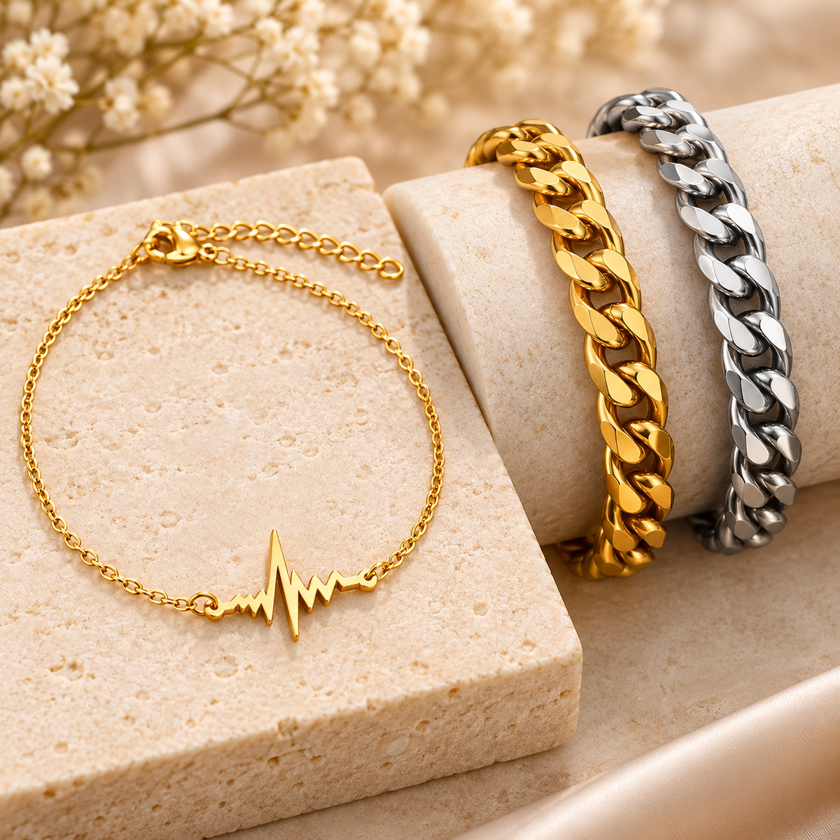 Gold and silver titanium bracelets featuring curb chains and a gold heartbeat bracelet displayed on cream stone.