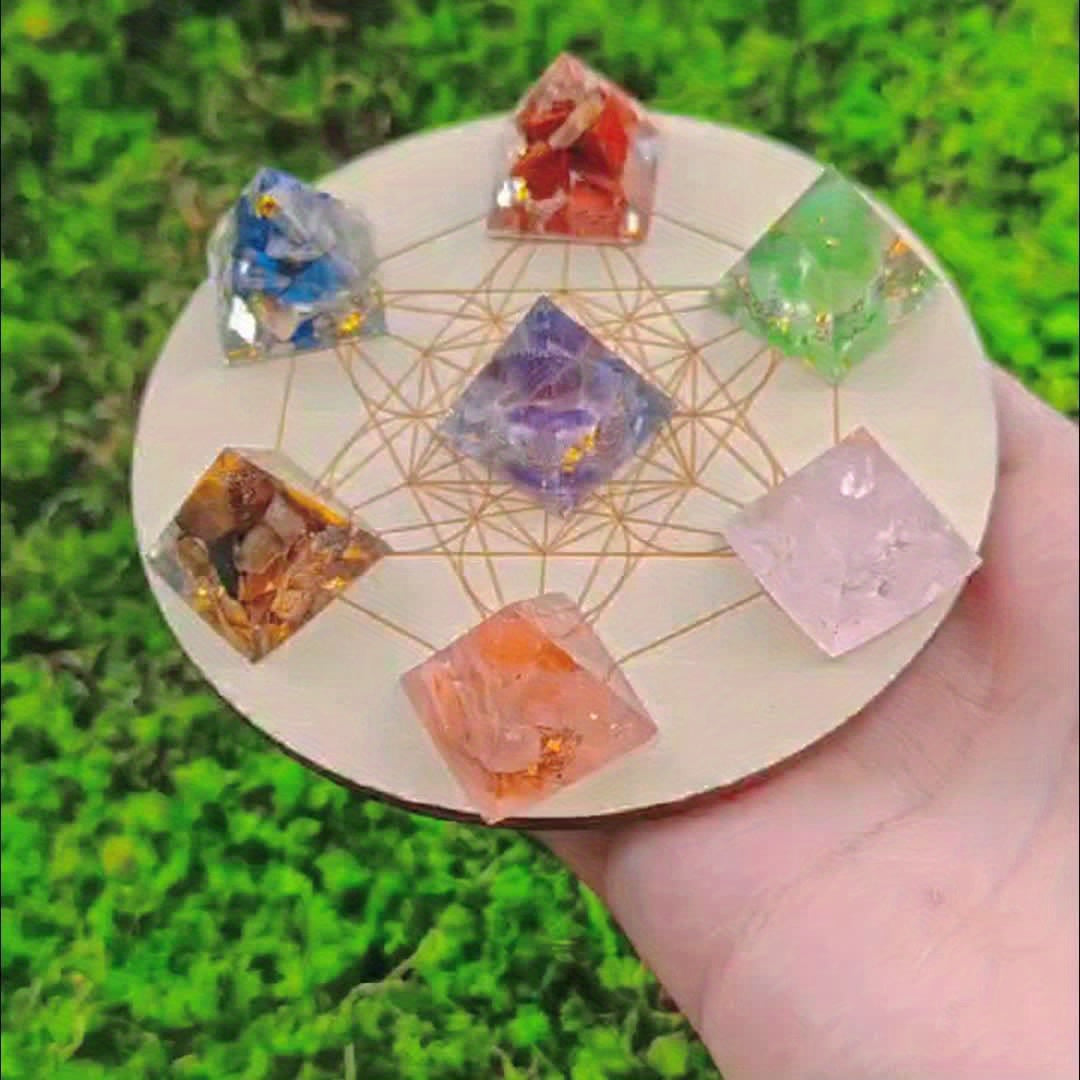 Outdoor image of a person holding the chakra pyramid set above green grass, with clear focus on the Metatron’s Cube layout and crystal colours.

