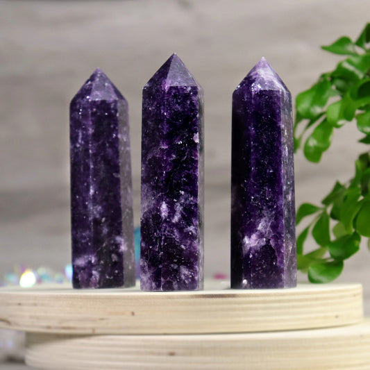 Three polished Lepidolite crystal towers standing on a round wooden platform, showcasing deep purple hues and white marbling for calming energy and chakra healing.