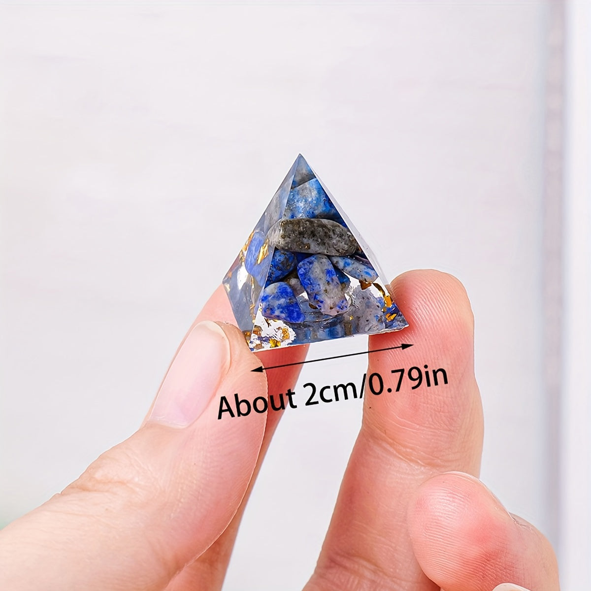 Close-up of a hand holding a small Lapis Lazuli orgone pyramid, showing its size of about 2cm with visible blue stones and gold foil.