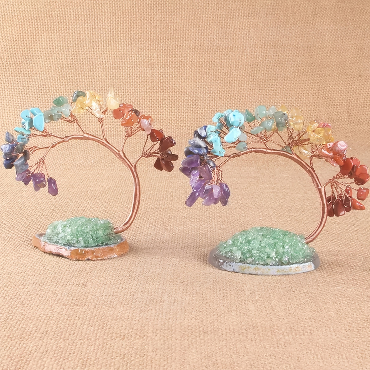 Two crystal chakra trees on textured fabric background with copper wire and gemstone branches, standing on druzy crystal bases.