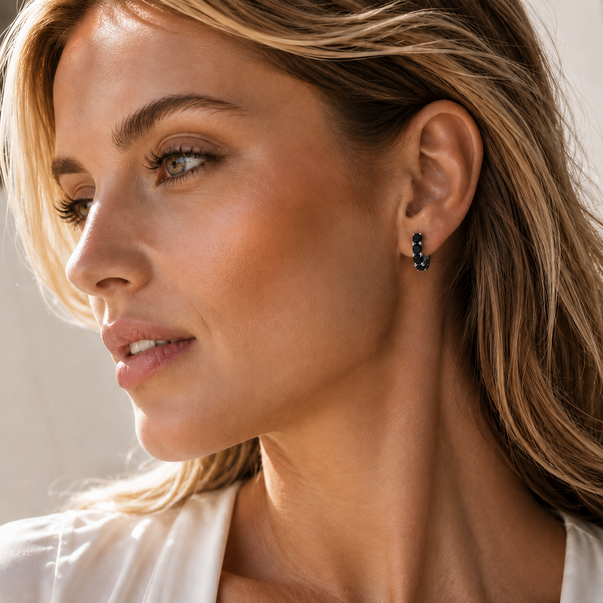 Gold five-stone hoop earring with black moissanite worn on the ear in a lifestyle close-up