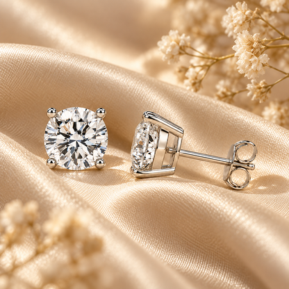 Silver four-prong colourless moissanite stud earrings displayed on champagne satin with dried flowers