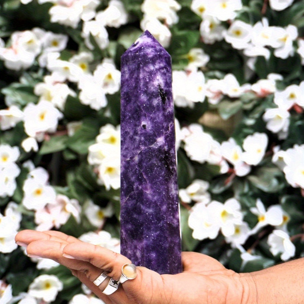 Hand holding a large Lepidolite tower against a background of white flowers, highlighting the stone’s rich violet colour and natural texture for anxiety relief and emotional balance.