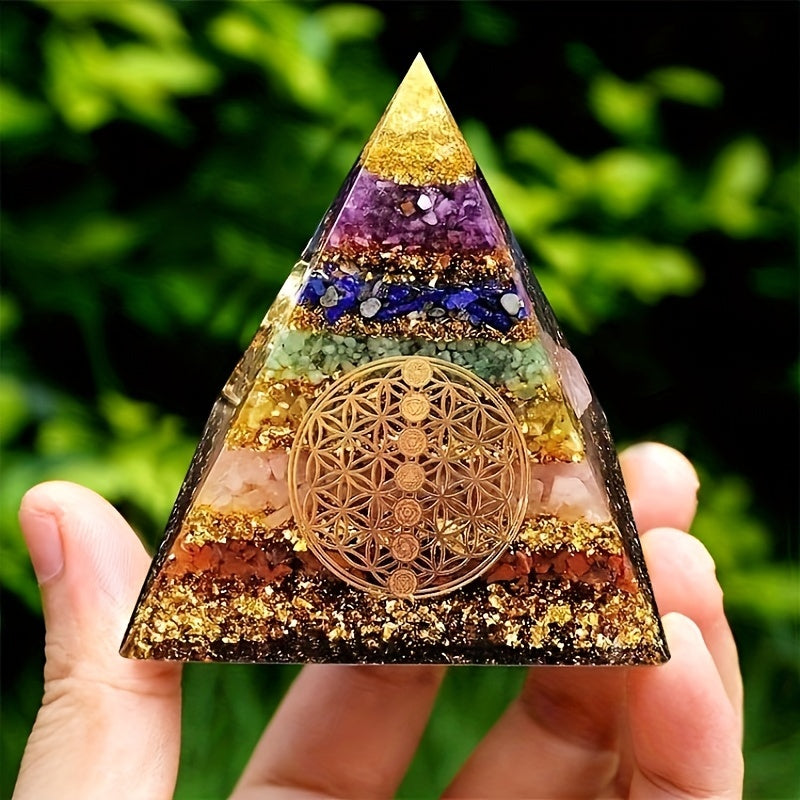 Hand displaying a 7 chakra orgone energy pyramid under natural light, highlighting colourful crystal layers and sacred geometry design.