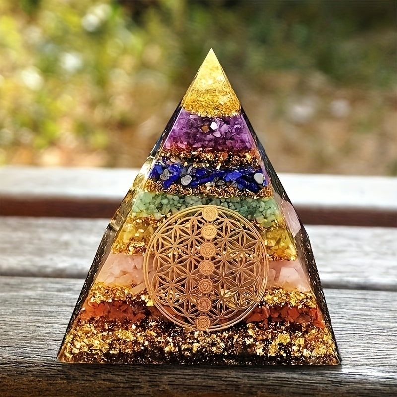 Chakra crystal orgone pyramid placed on a wooden surface outdoors, showcasing gemstone layers and gold leaf accents for energy healing.