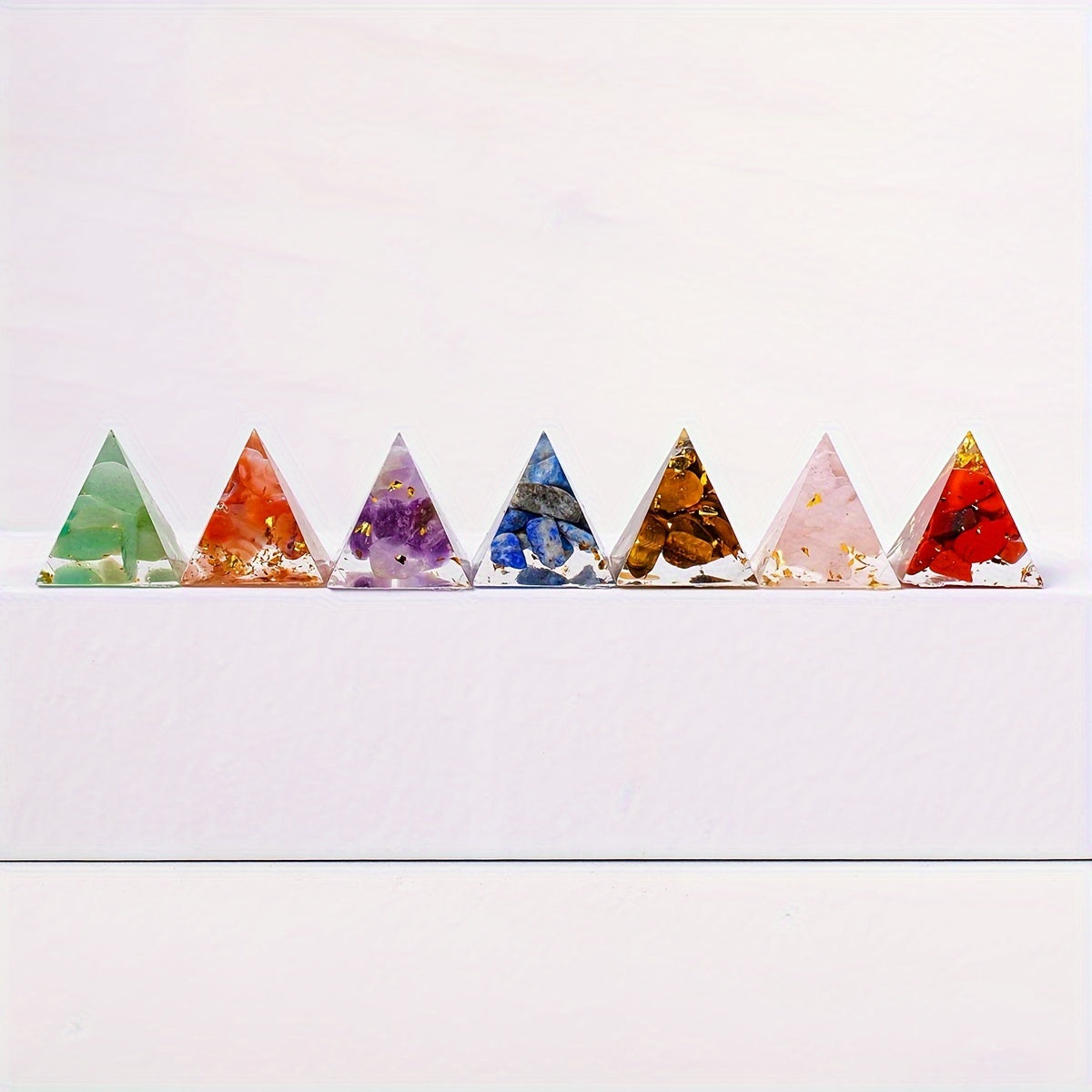 Front-facing lineup of seven chakra orgone pyramids in a row on a white surface, showcasing natural crystals for energy balance and healing.