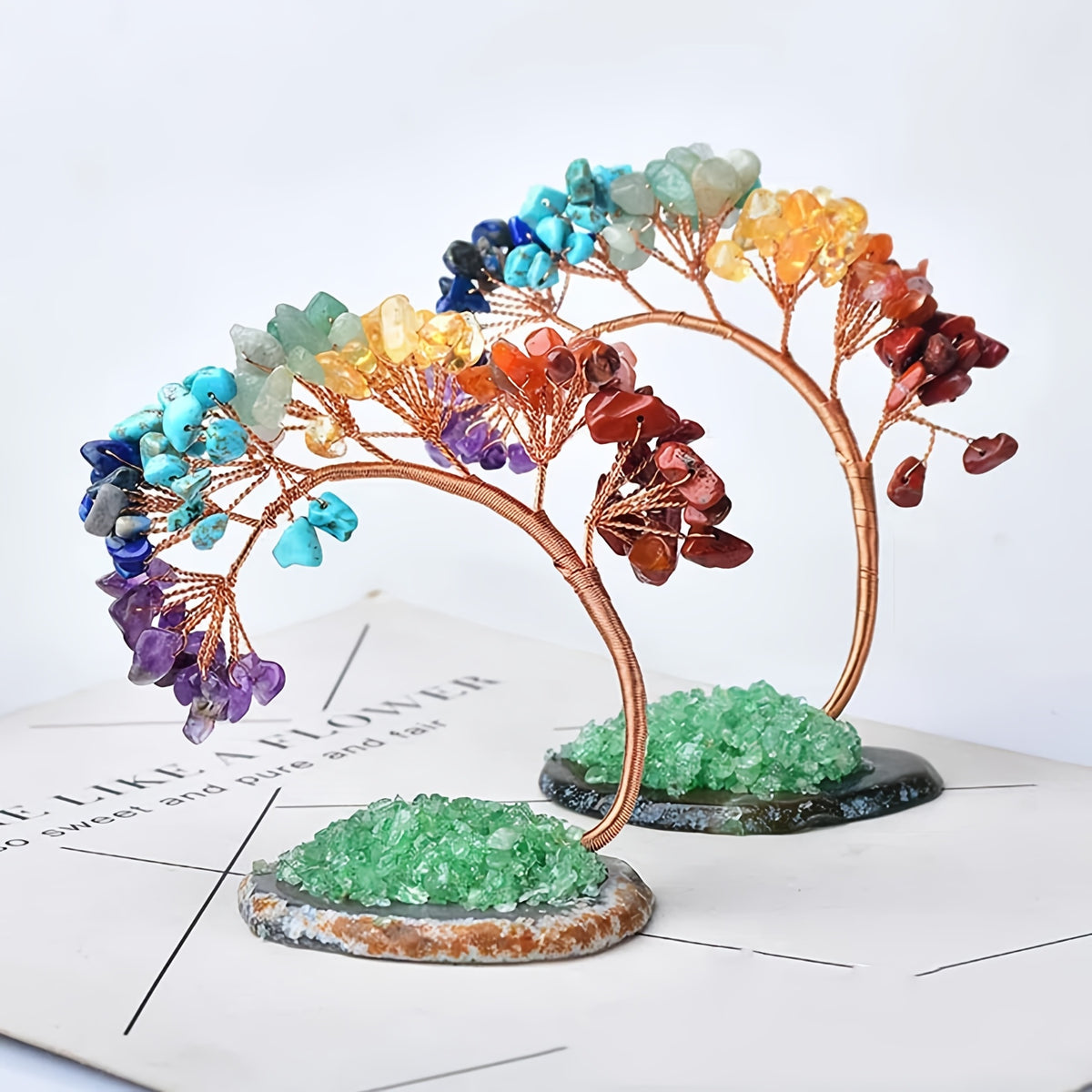 Pair of chakra crystal bonsai trees with green crystal bases and gemstone leaves arranged in rainbow gradient, displayed on a white surface.