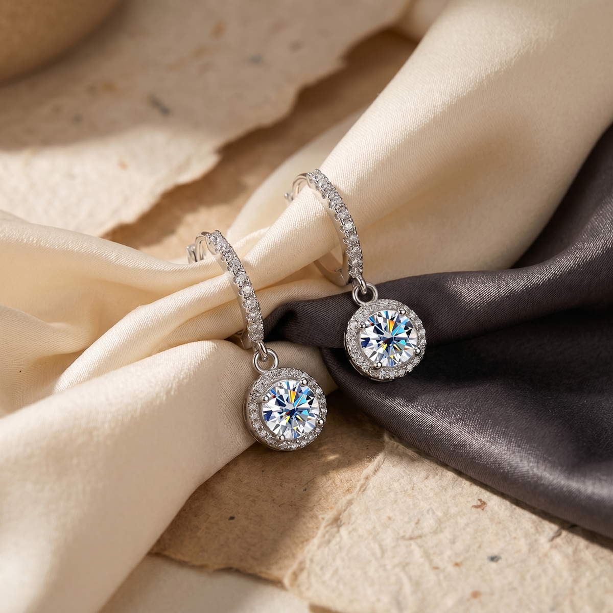 Silver halo colourless moissanite hoop drop earrings arranged on cream and black fabric