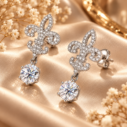Silver fleur de lis colourless moissanite drop earrings displayed at an angle on champagne satin
