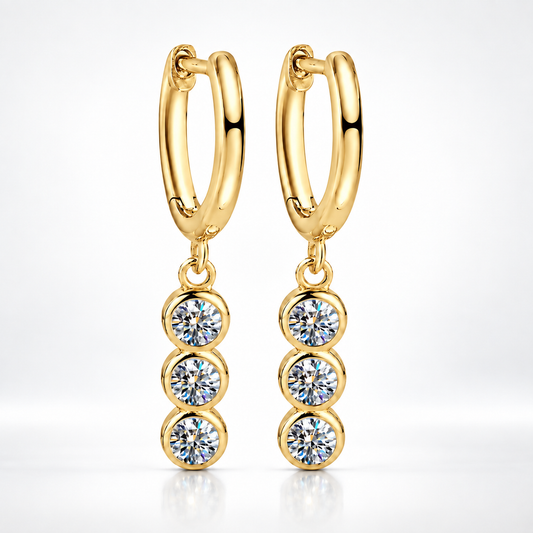 Gold huggie hoop earrings with three bezel-set round moissanite drops on a white background
