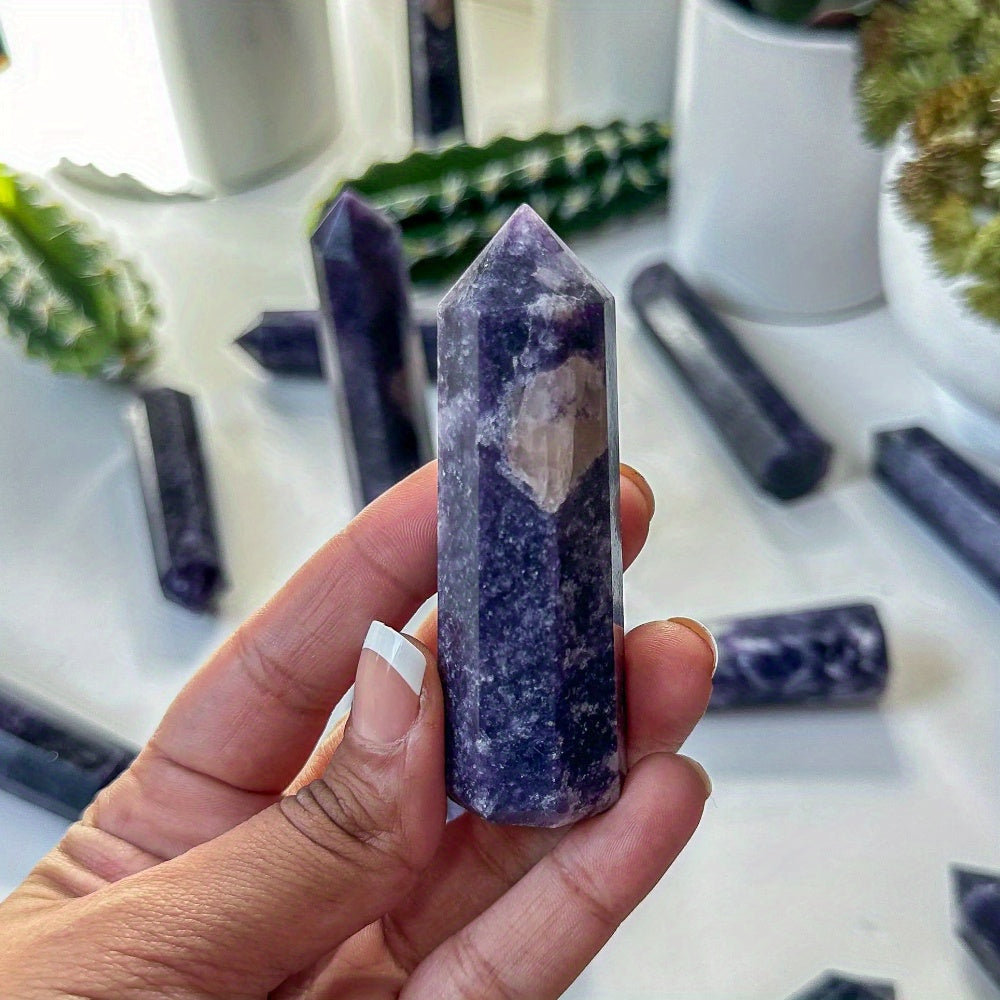 Close-up of a Lepidolite tower with a raw inclusion, held in hand among potted plants, perfect for inner calm and spiritual growth practices.