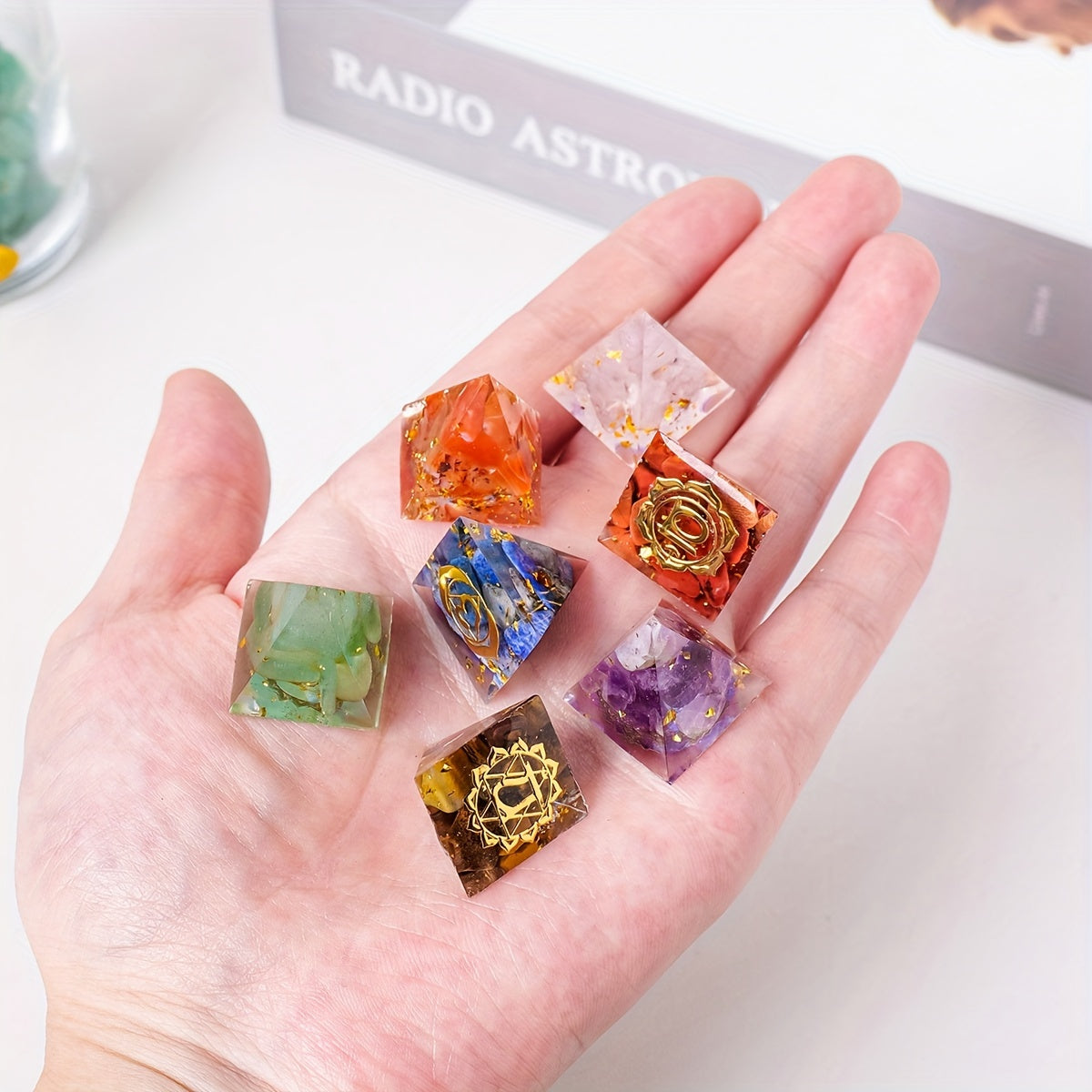 Hand holding seven mini chakra crystal pyramids, revealing embedded golden chakra symbols on some pyramids including Amethyst and Carnelian.