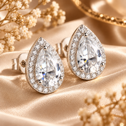 Silver pear-cut halo moissanite stud earrings displayed on champagne satin with flowers