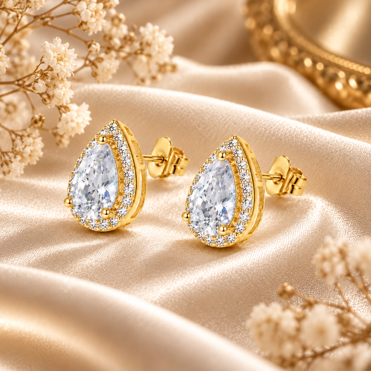 Gold pear-cut halo moissanite stud earrings displayed on champagne satin with flowers
