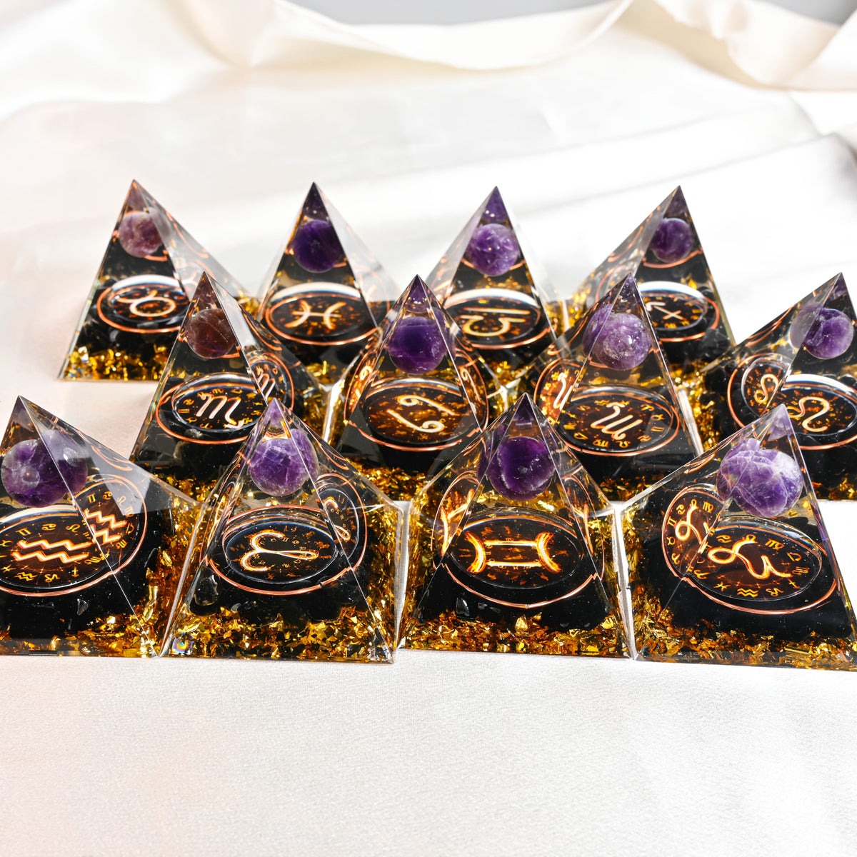 Complete set of twelve orgone pyramids with all zodiac signs arranged in a grid on satin fabric.