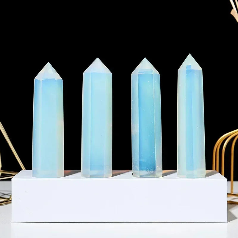 Four polished opalite crystal towers with a milky blue iridescence, standing on a white display base against a black background. Used for emotional clarity and spiritual communication.