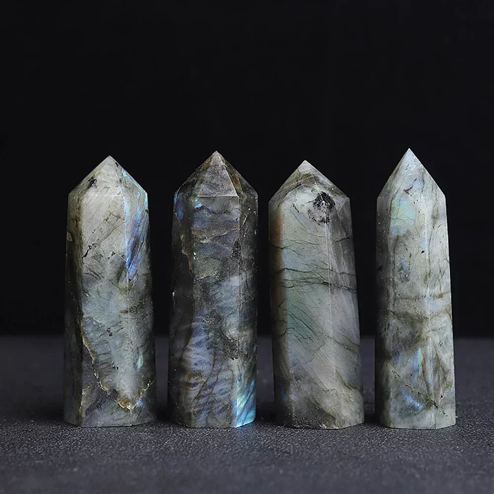 Four labradorite crystal towers showcasing flashes of blue and green iridescence on a grey base, standing against a dark backdrop. Used for transformation, intuition, and shielding.