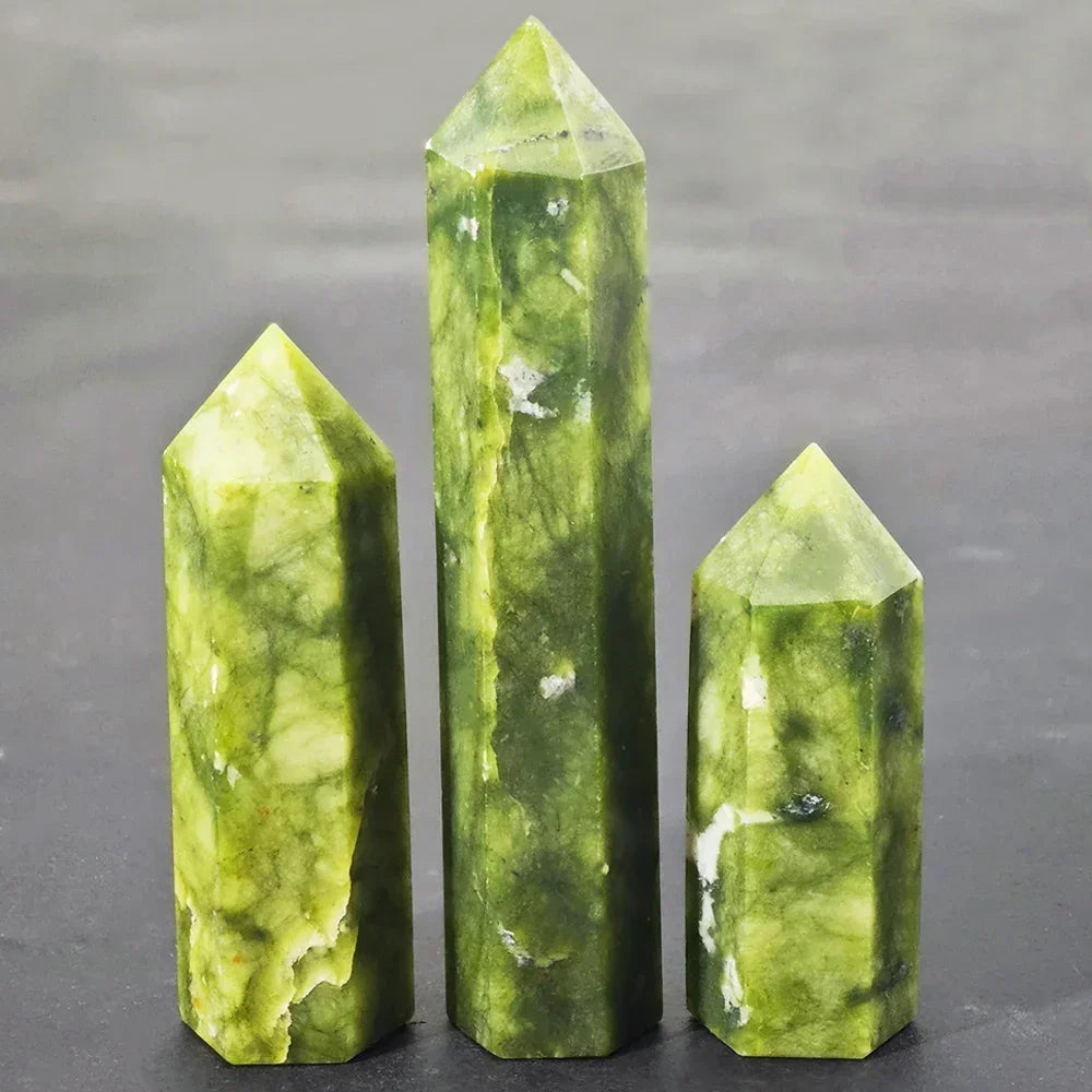 Three Xiuyan jade towers in varying shades of light to deep green, standing upright on a neutral grey background. Traditionally used for abundance, healing, and emotional balance.