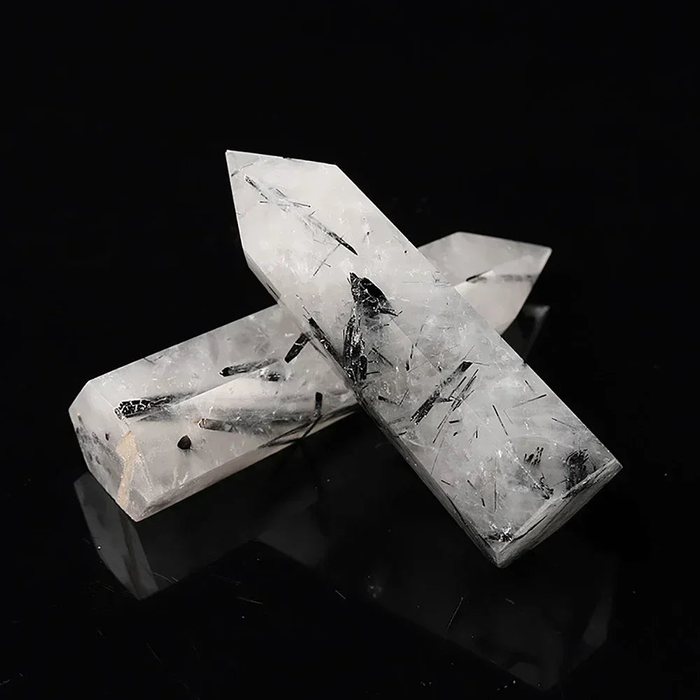 Two black tourmaline in quartz towers featuring clear white quartz with striking black needle-like inclusions, laid across one another on a reflective black background. Excellent for protection and energy purification.
