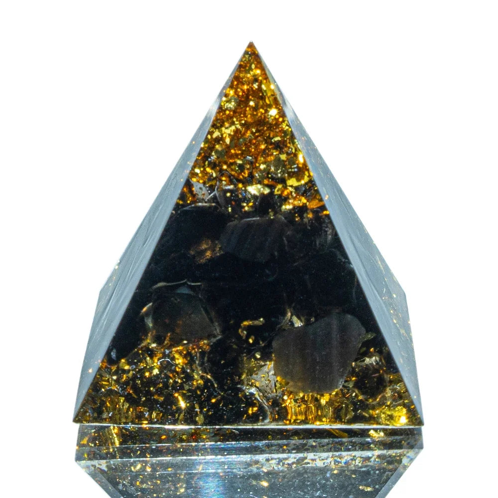 A 3cm orgone pyramid with deep black obsidian stones encased in clear resin and accented with shimmering gold foil, crafted for grounding, protection, and EMF shielding.