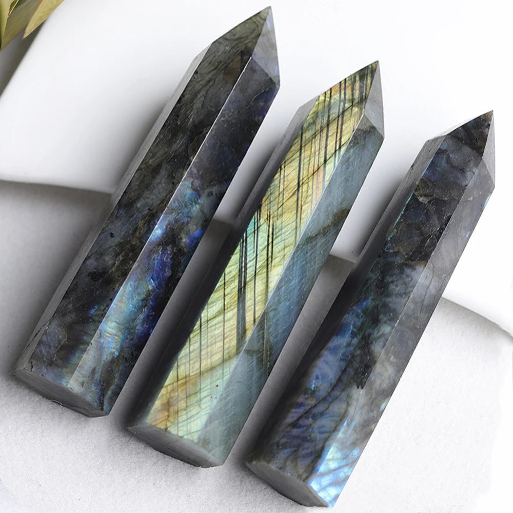 Three polished labradorite crystal towers lying diagonally on a soft surface, showcasing striking iridescent reflections in blue, green, and gold.