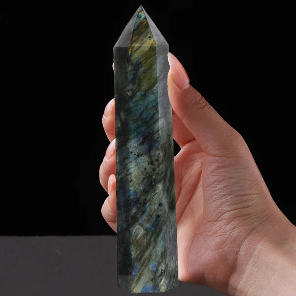 Hand holding a large labradorite point crystal with vivid labradorescence on a black background.
