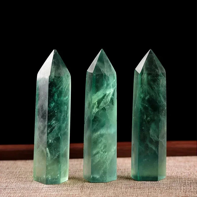 Three translucent green fluorite crystal towers with natural veining, standing on a beige mat with a black background. Associated with cleansing, renewal, and heart chakra healing.
