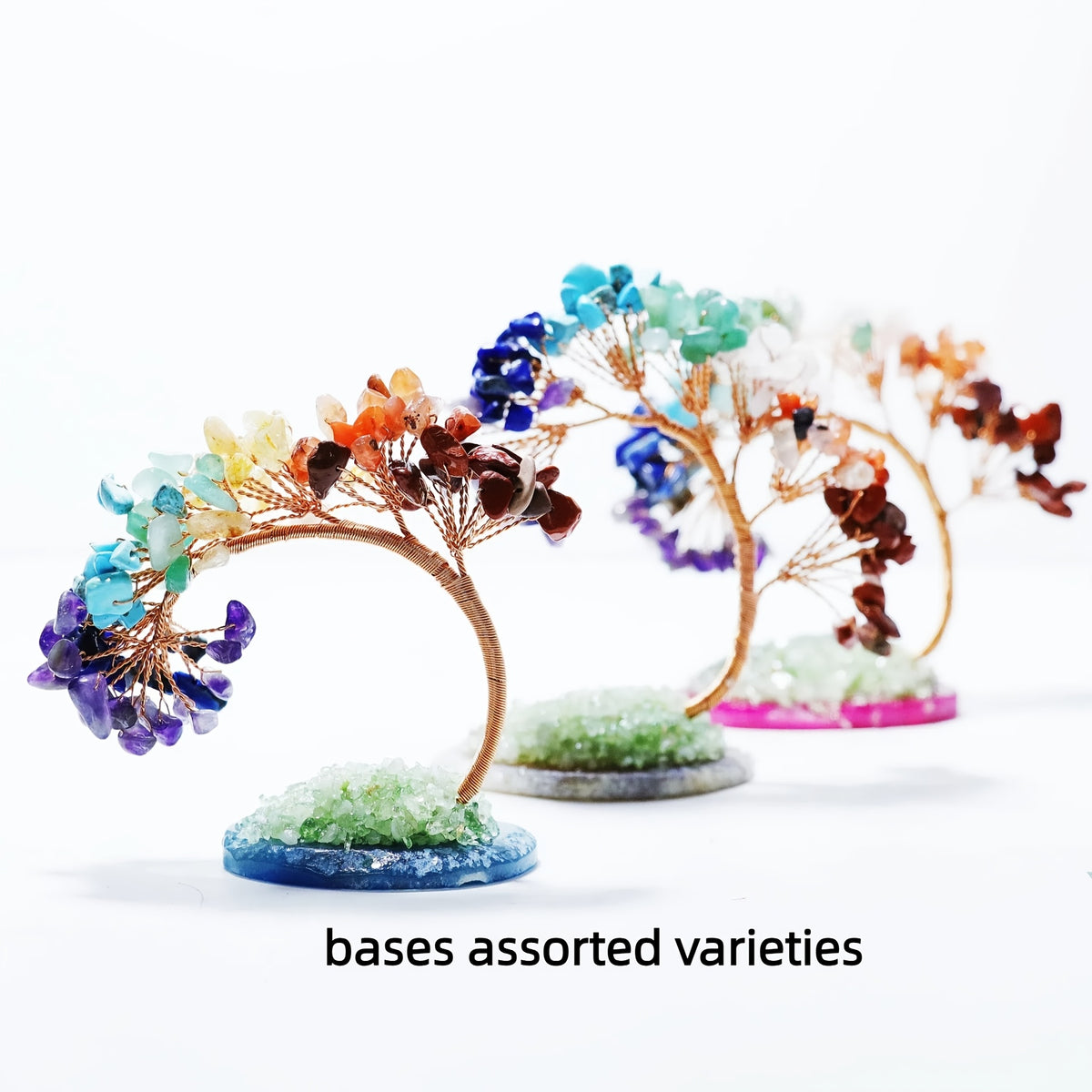 Row of chakra gemstone bonsai trees with arched copper wire trunks and colourful crystal leaves on assorted bases, text 'bases assorted varieties' below.