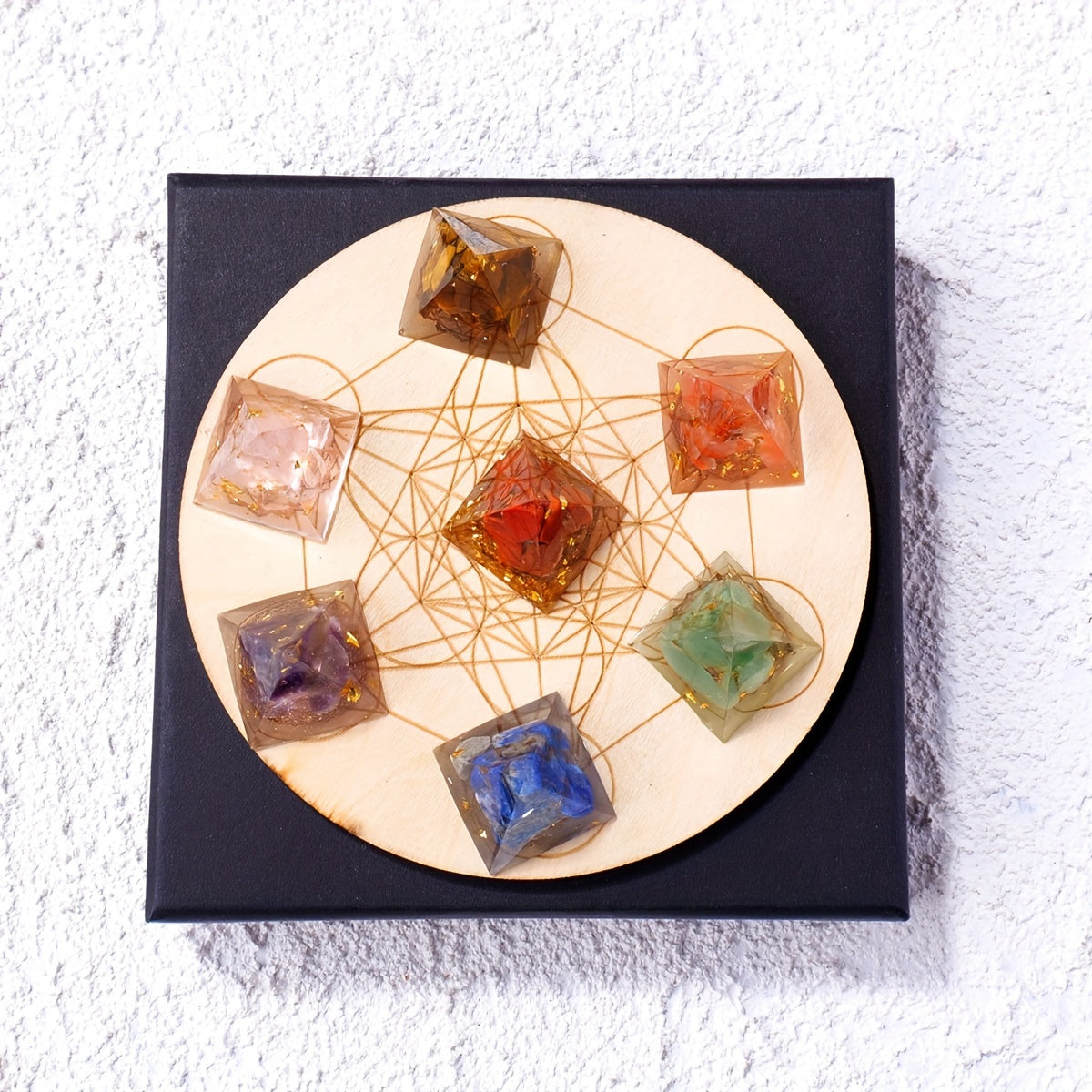 Top view of 7 Chakra Orgone Pyramids on a wooden Metatron’s Cube grid over a black box, featuring Amethyst, Lapis Lazuli, Tiger Eye, Rose Quartz, Red Jasper, Green Aventurine, and Carnelian.